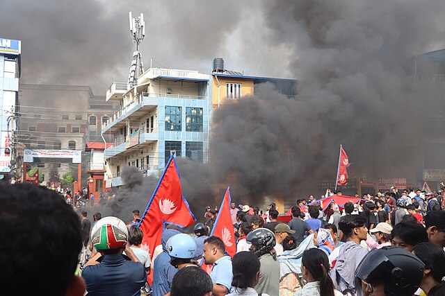 a crowd in Nepal watching as a government building burns