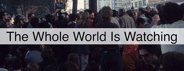 a crowd, with a banner that says 'the whole world is watching'